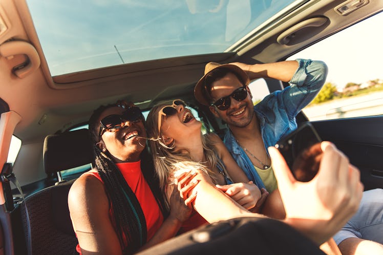 Three best friends enjoying traveling in the car, sitting in rear seat and having lots of fun making...