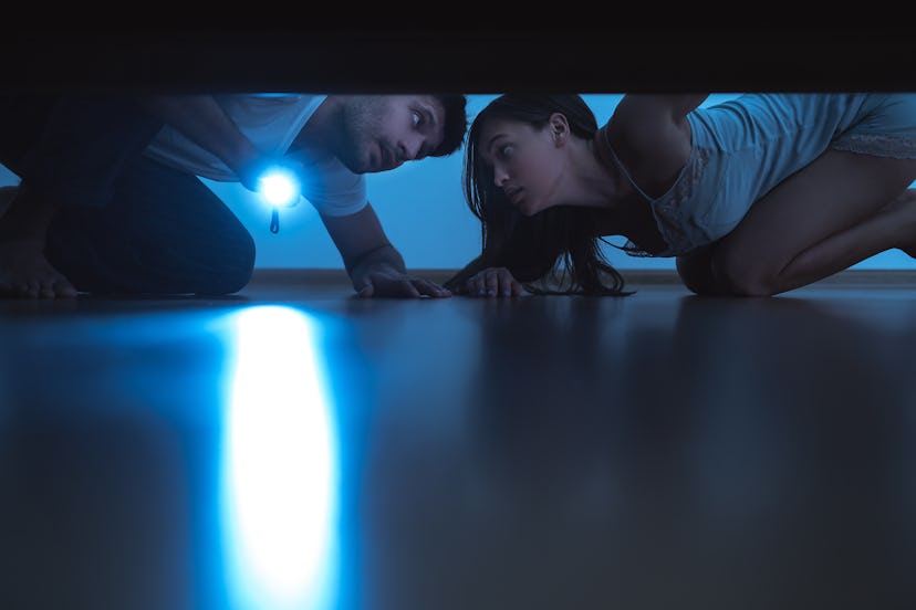 The man and a woman with a flashlight looking under the bed. evening night time