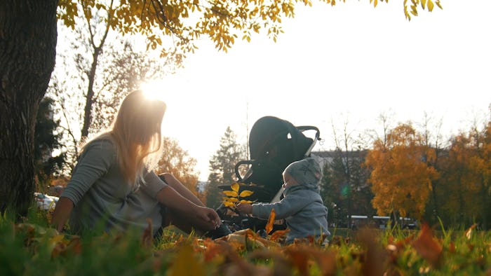 Young mother playing with leaves with her laughing little baby in autumn park