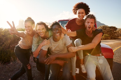 Five millennial friends on a road trip have fun posing for photos at the roadside, lens flare