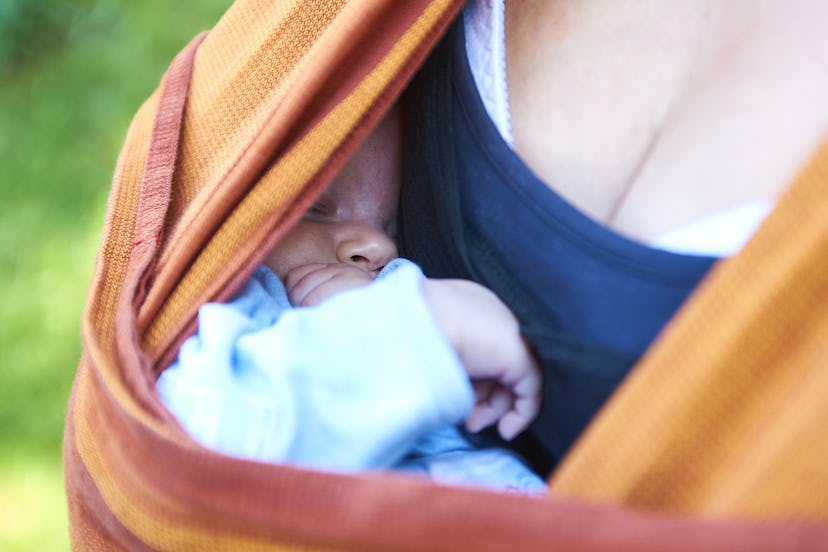 Unrecognizable young mother with her baby daughter hidden in sling outside in nature
