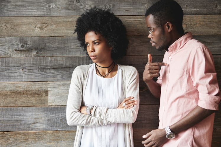 Dark-skinned man standing next to his offended wife with Afro haircut and crossed arms, man looking ...