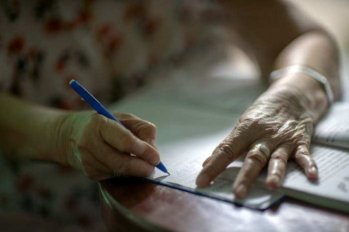 blue ballpoint pen in the hands of the old woman Is writing a book on a wooden table There is a ligh...