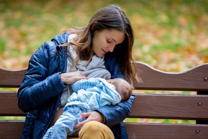 Young mother, breastfeeding her newborn baby boy outdoor in the park, autumn time