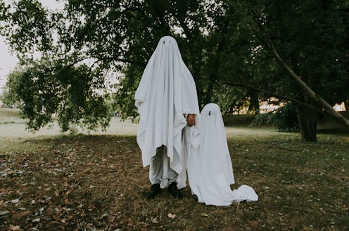 Father and son playing ghosts with white sheets in the garden, conceptual photos about halloween hol...