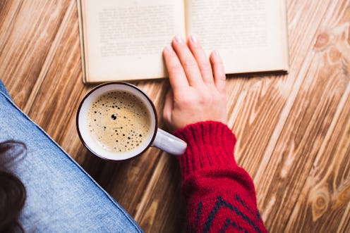 young woman in a red sweater holding a cup of coffee and reading a book