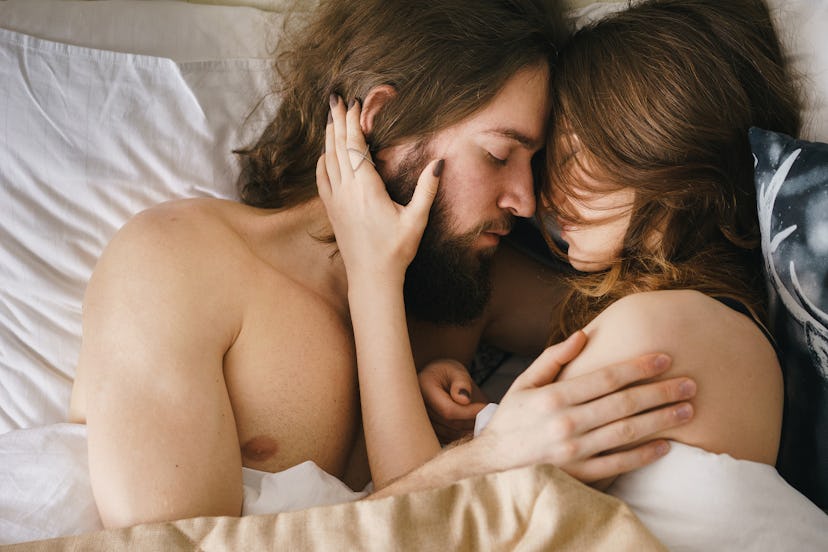 From above shot of young naked couple embracing in bed with eyes closed. 