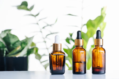 Transparent cosmetic amber glass dropper bottles over green plants on white background. Vials with p...