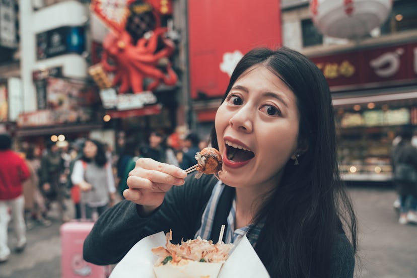 korean female model tourist eating octopus ball dumpling showing face camera open wide mouth. happy ...