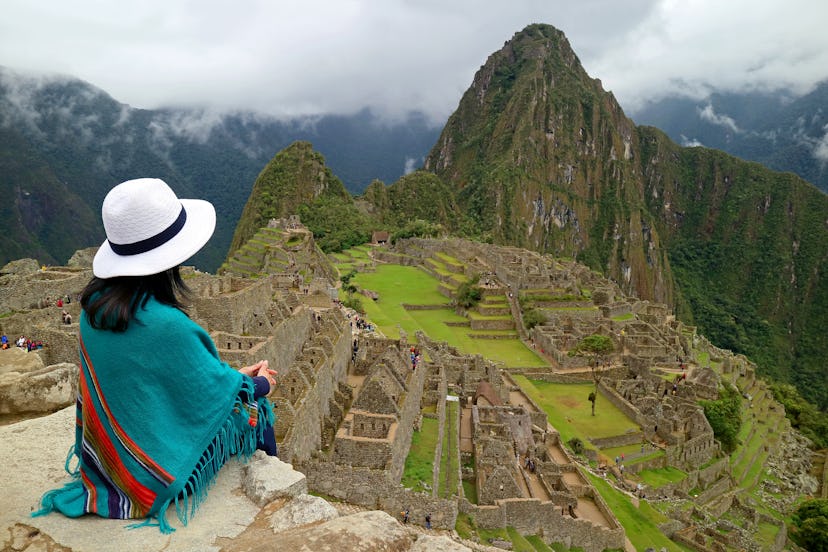 Female Traveler Sitting on the Cliff Looking at the Inca ruins of Machu Picchu, UNESCO World Heritag...