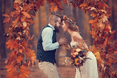 Beautiful bridal couple, bearded bride and groom in a wreath, laughing happily in the arch of autumn...