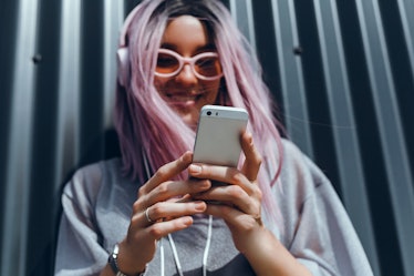 A happy girl with pink hair and headphones looks at her phone. 