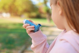 Little girl using asthma inhaler outdoors. Health care