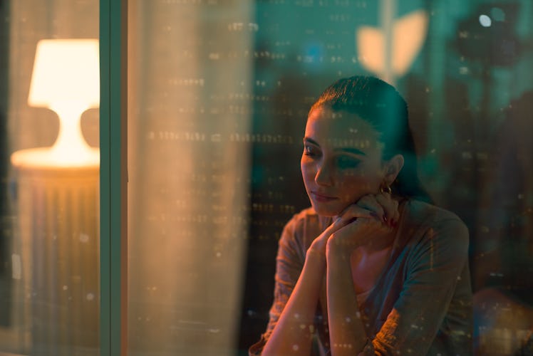 Sad lonely woman sitting next to a window, she is looking down and thinking