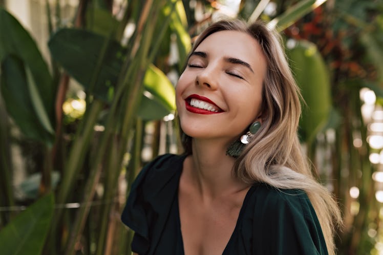 Happy smiling woman with white teeth and red lips feeling happiness while walking outside on the isl...