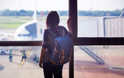 Young  tourist woman in the airport, looking through the window at plane
