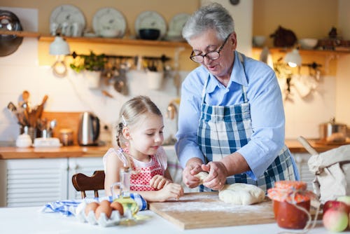 Family is cooking in cozy kitchen at home. Grandmother is teaching little girl. Senior woman and chi...