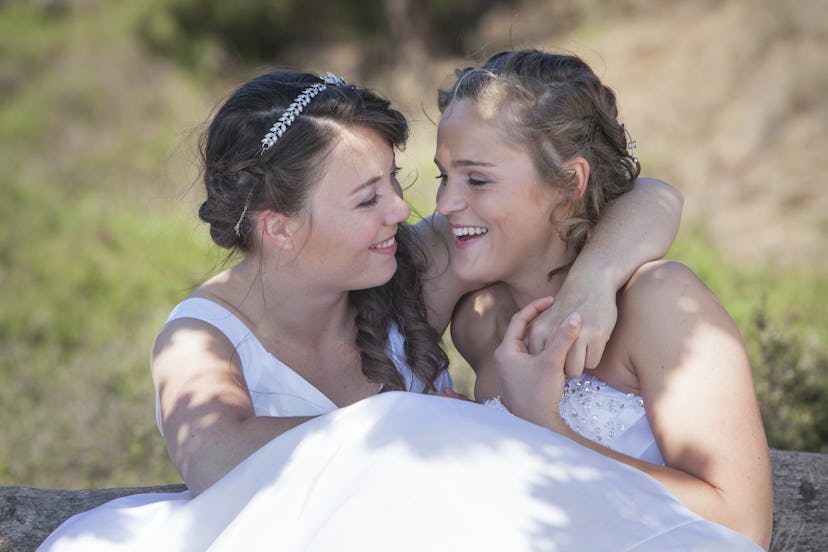 two brides smile and embrace in nature surroundings on sunny day