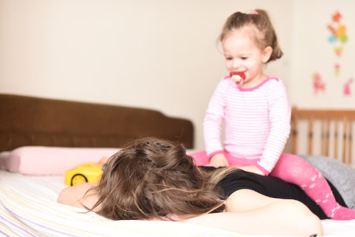 horizontal portrait of a little girl sitting on her mother's back while she sleeps in the bedroom on...