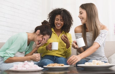 Diverse roommates drinking coffee, eating cookies and laughing at home