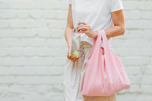 Female hands hold eco bag   and reusable water bottle. Zero waste. Sustainable lifestyle concept.