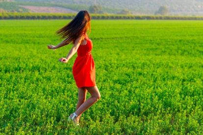 Young woman happily twirling in her summer red dress. Girl Spinning in a green field at sunny day. H...