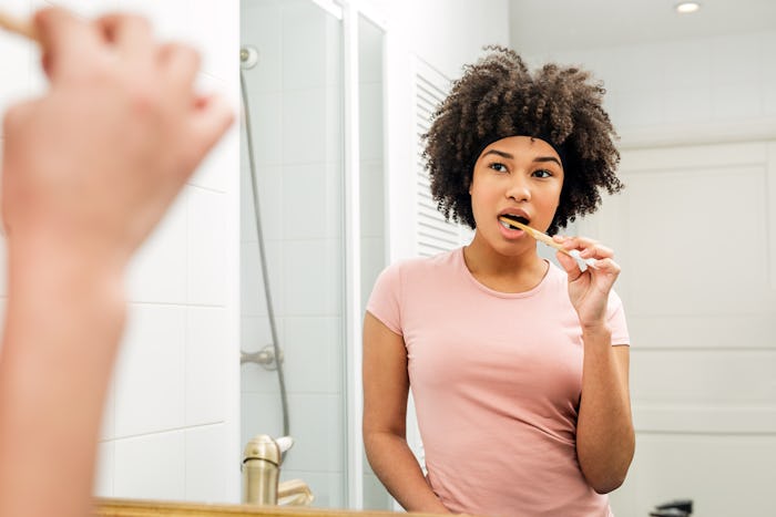 Woman brushing her teeth. Girl with bamboo brush in front of the mirror.