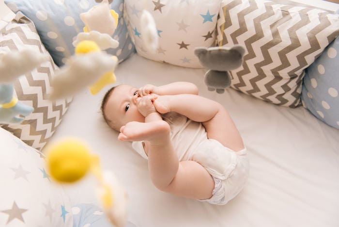 Cute baby lies in a white round bed. Light nursery for young children. Toys for infant cot. Smiling...