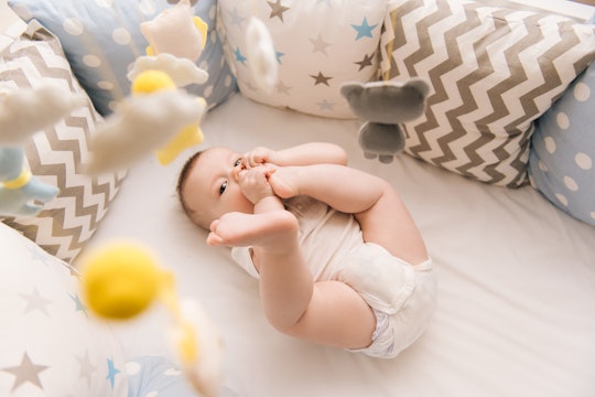 Cute baby lies in a white round bed. Light nursery for young children.  Toys for infant cot. Smiling...