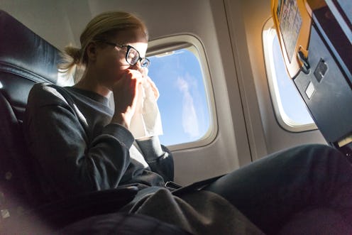 Blonde caucasian woman sneezing while flying by commercila airplane.