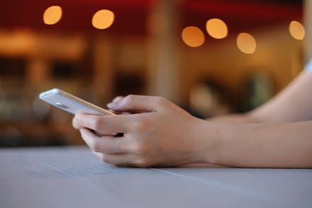 Hand of woman and smartphone on white wooden table,Space for text or design.