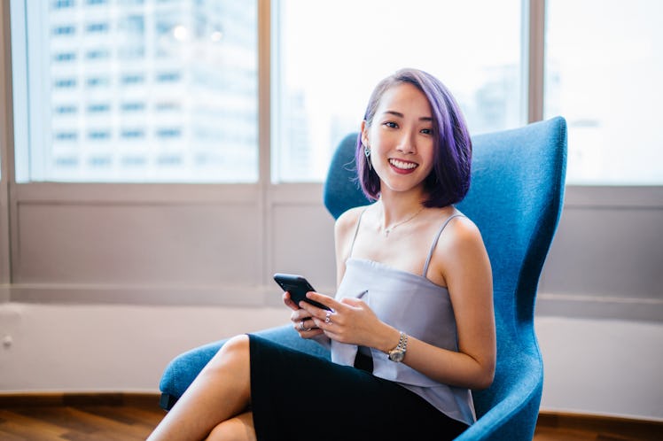 Business portrait of a young, slim, elegant and beautiful Asian business woman sitting in a blue arm...