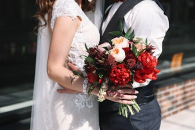 Wedding couple is holding wedding bouquet with peonies, roses and red flowers and greenery in her ha...