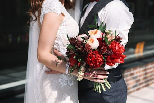 Wedding couple is holding wedding bouquet with peonies, roses and red flowers and greenery in her ha...