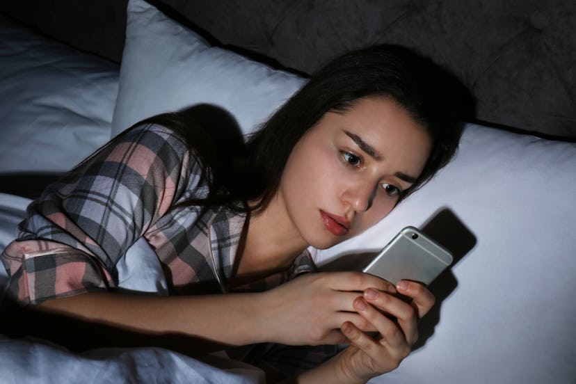Sad lonely woman using smart phone in bed