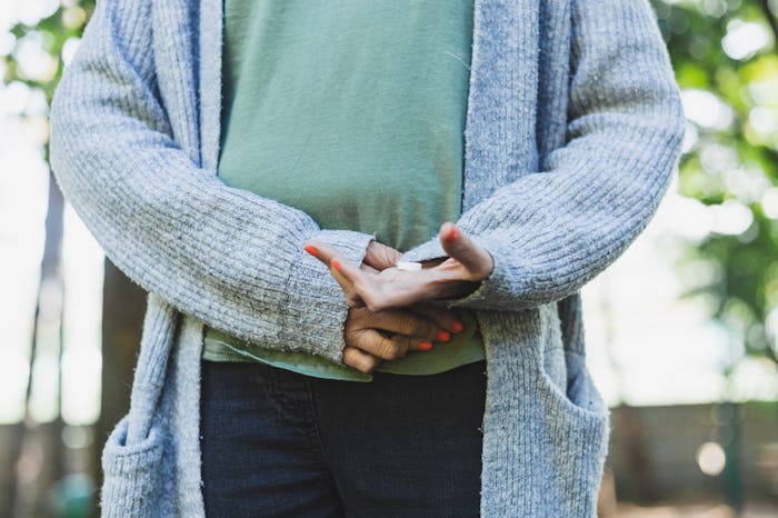 Young woman with period pain while holding painkiller and one hand on her belly outdoor - Casually d...