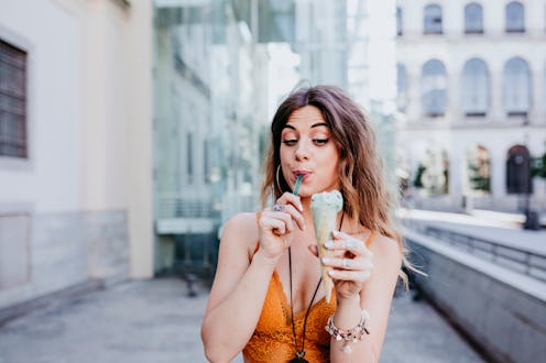 Beautiful young caucasian woman eating mint ice cream at the city street on a sunny day. Happy face ...