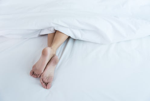 Under white blanket covers with feet showing on bed at home