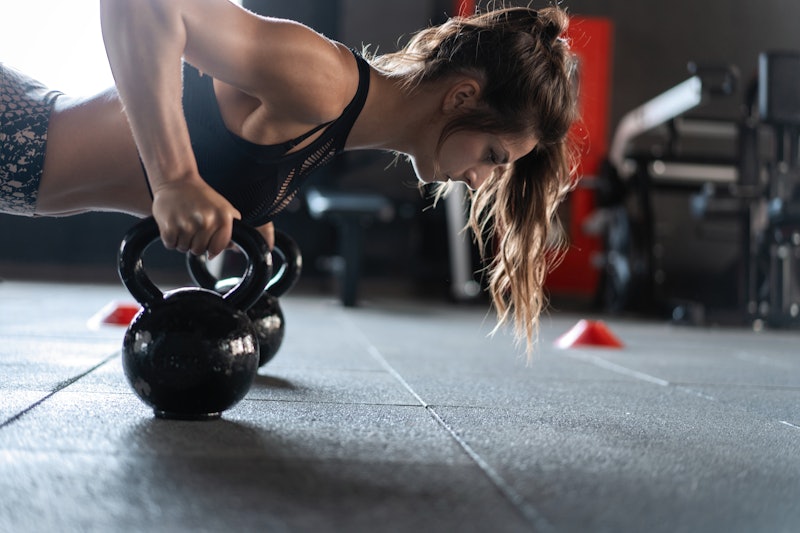 Sportive woman doing push-ups in the gym using kettlebells