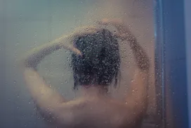 Naked girl takes a shower after the misted glass
