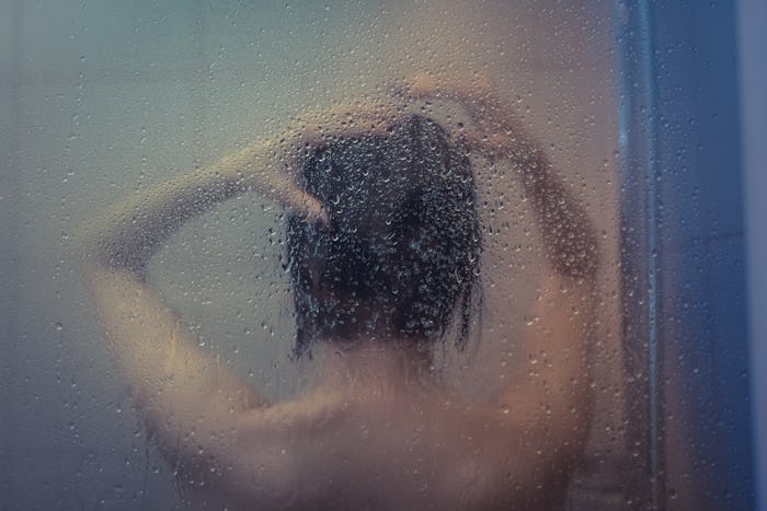 Naked girl takes a shower after the misted glass