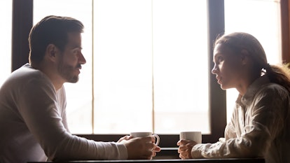 Serious man and woman sitting at cafe table drinking coffee talking and chatting, millennial colleag...