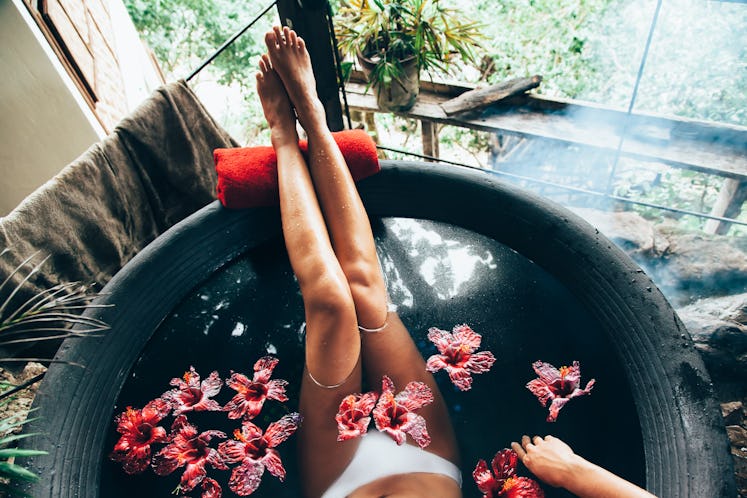 Woman relaxing in round outdoor bath with tropical flowers. Organic skin care in kawa hot bath in lu...