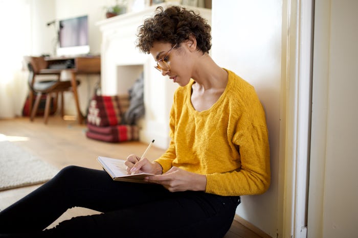 Portrait of young african american woman sitting on floor writing ideas into book