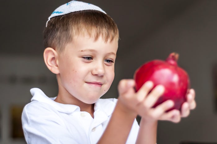 Cute Caucasian kid holding a ripe pomegranate fruit in his hands. Rosh Hashanah, Jewish New Year hol...