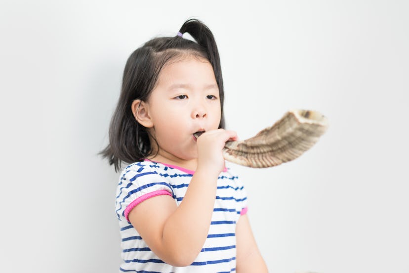 Little girl blowing the Shofar (horn) of Rosh Hashanah (New Year) on white background. Religious sym...