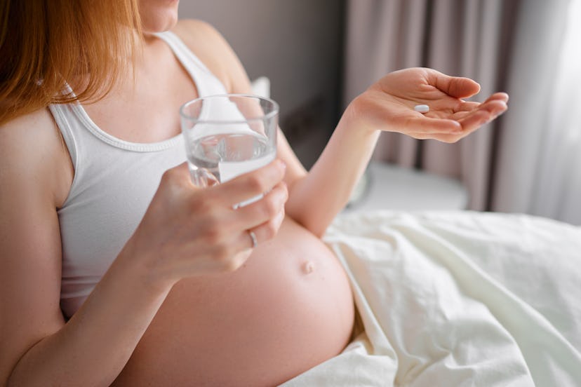 Medicine and pragnancy. Young pregnant woman holding pill and glass of water in her hand.