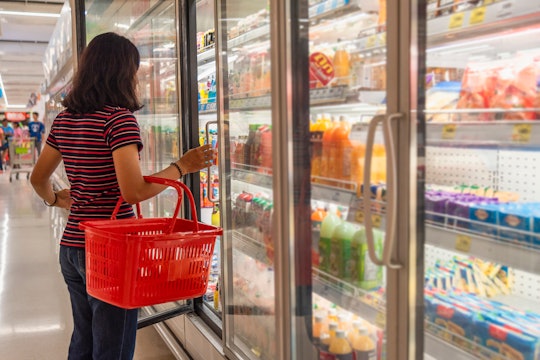 A girl with a basket takes frozen foods from the supermarket's refrigerator. The girl chooses goods ...