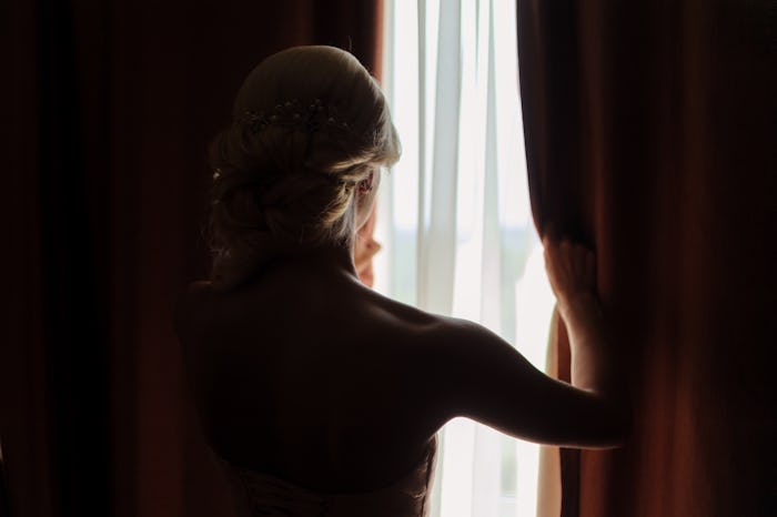 The bride looks out the window, opening the curtain. waiting for the groom. the view from the back