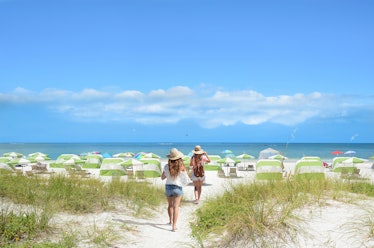 Girls walking on the beach on summer vacation.  Beach chairs and parasols on beautiful white sand in...